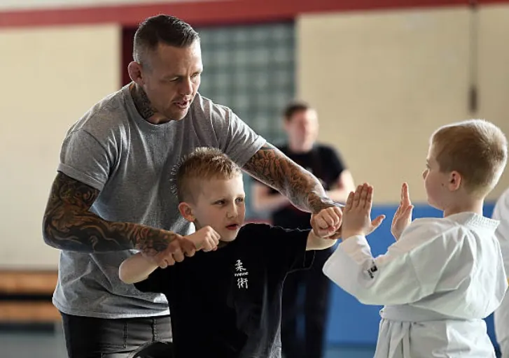 Coach teaching two young students a guard position on the mats