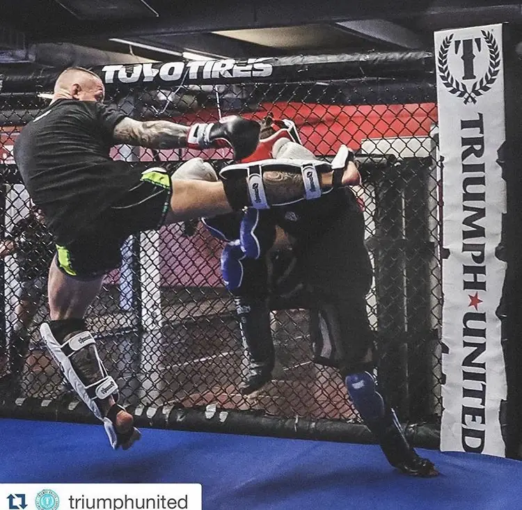 Fighter landing a high kick on his partner inside a caged ring